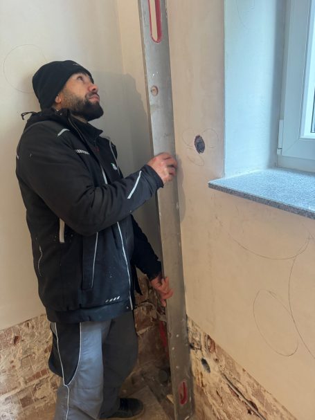 Mann hält eine Wasserwaage an die Wand in einem renovierten Raum.