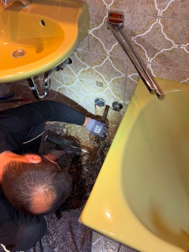 Freilegung der Schadstelle Fachmann untersucht eine freigelegte Wasserleitung zwischen Waschbecken und Badewanne.