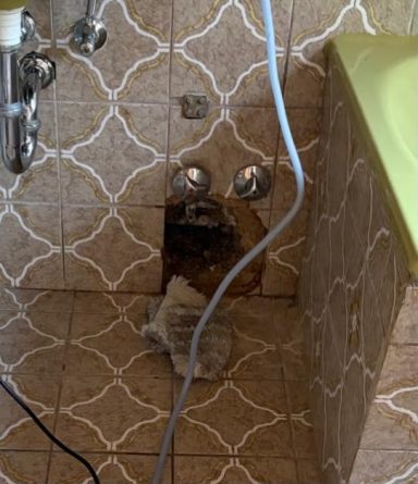 Geöffneter Leitungsbereich Geöffnete Fliesenwand mit freigelegtem Leitungsbereich neben einer Badewanne.
