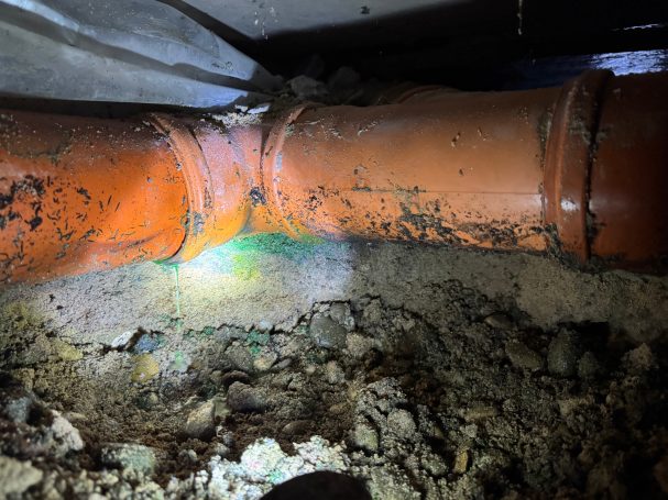 Leckageortung am Abflussrohr mit fluoreszierender Prüffarbe. Wasseraustritt aus einem undichten Abflussrohr, sichtbar gemacht mit fluoreszierender Prüffarbe.